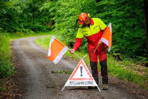 Ein Waldarbeiter stellt ein Warnschild mit Warnfähnchen auf einem Waldweg auf