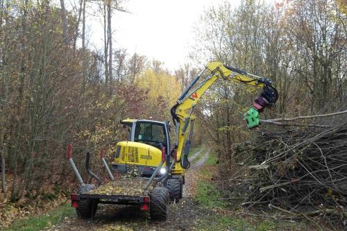 Minibagger lagert das abgezwickte Material am Wegrand auf einen Reisighaufen ab